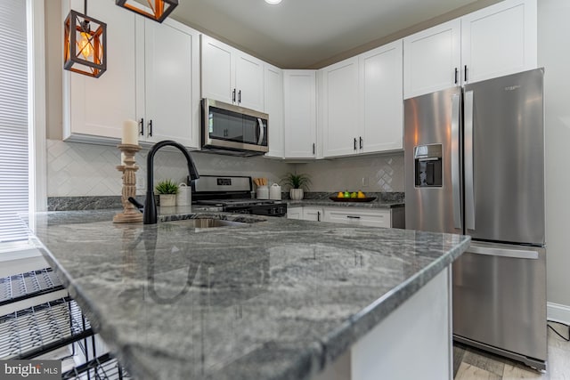 kitchen featuring appliances with stainless steel finishes, a sink, dark stone countertops, tasteful backsplash, and white cabinets