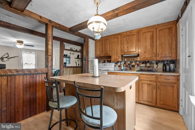 kitchen featuring light wood finished floors, beamed ceiling, light countertops, backsplash, and brown cabinetry