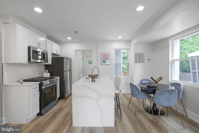 1456 Congress Pl SE, Washington, DC 20020 - kitchen with stainless steel appliances, a sink, white cabinets, light stone counters, and an island with sink