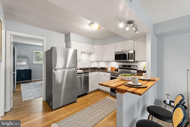 122 N Bedford St Unit A, Arlington, VA 22201 - kitchen featuring stainless steel appliances, a textured ceiling, white cabinetry, light wood-style floors, and tasteful backsplash