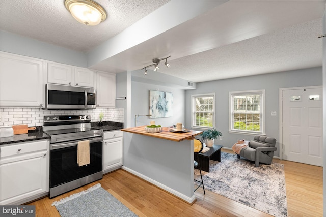 122 N Bedford St Unit A, Arlington, VA 22201 - kitchen with appliances with stainless steel finishes, a textured ceiling, light wood-style floors, white cabinets, and backsplash