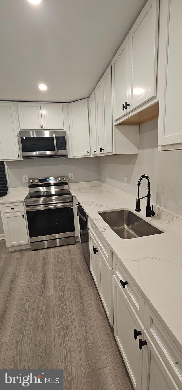 5303 55th Pl, Riverdale, MD 20737 - kitchen featuring stainless steel appliances, a sink, white cabinetry, wood finished floors, and light stone counters