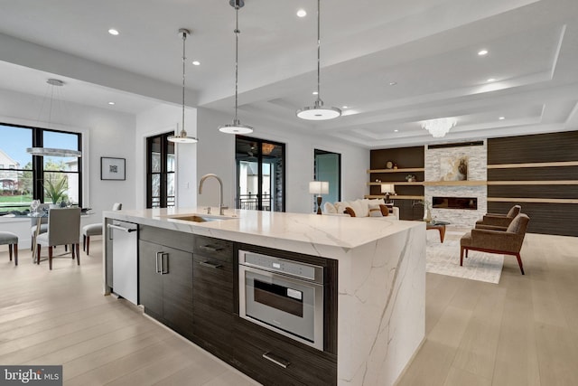 kitchen with a sink, light wood-style flooring, built in shelves, recessed lighting, and a center island with sink