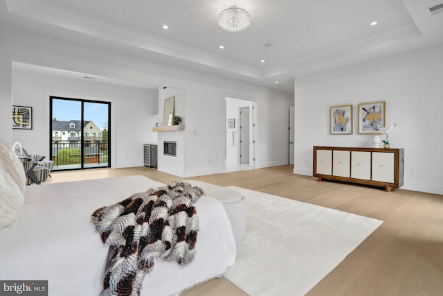 bedroom with access to exterior, a raised ceiling, wood finished floors, recessed lighting, and a chandelier