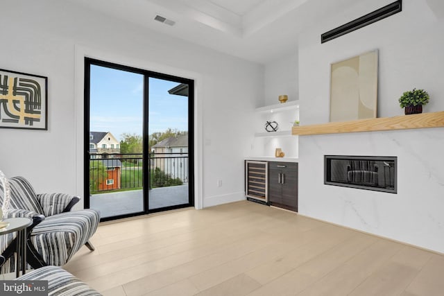 living room with a bar, beverage cooler, light wood-style flooring, and built in shelves