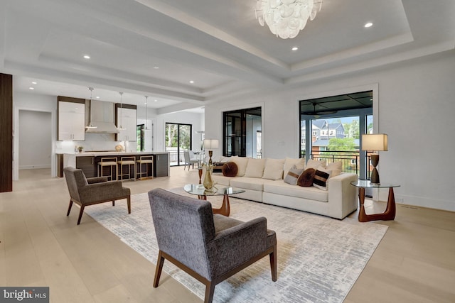 living room featuring a raised ceiling, a chandelier, baseboards, light wood-type flooring, and recessed lighting