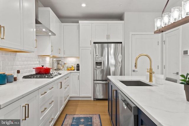 kitchen featuring appliances with stainless steel finishes, a sink, white cabinetry, light wood finished floors, and light stone countertops
