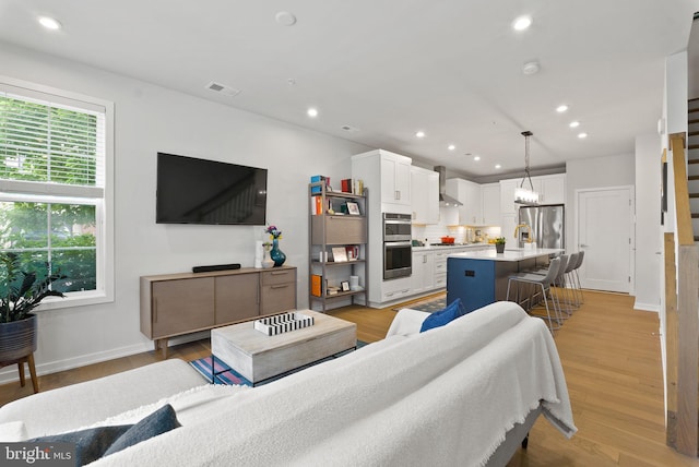 living area featuring recessed lighting, light wood-type flooring, baseboards, and stairway