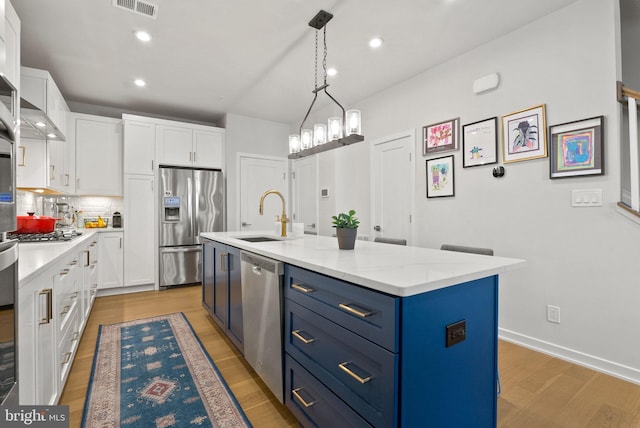 kitchen with stainless steel appliances, a sink, blue cabinets, white cabinets, and recessed lighting