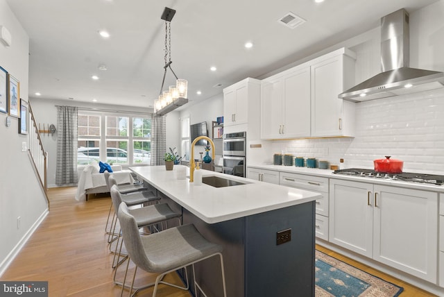 kitchen featuring wall chimney exhaust hood, a sink, stainless steel appliances, recessed lighting, and backsplash