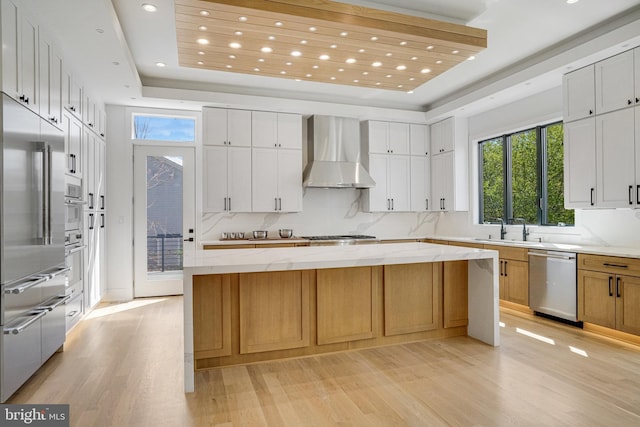 kitchen featuring wall chimney range hood, stainless steel appliances, light wood-type flooring, a sink, and recessed lighting