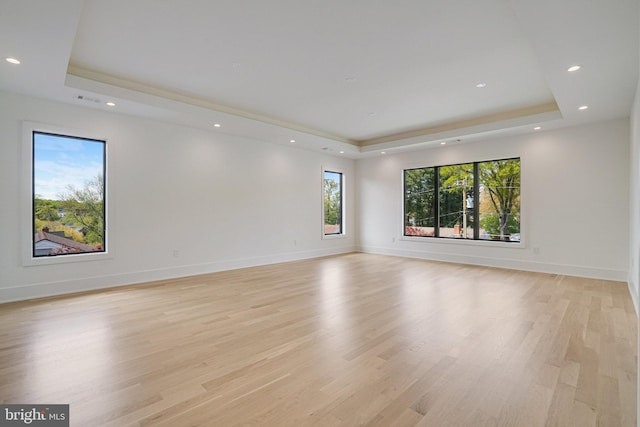spare room featuring a raised ceiling, recessed lighting, light wood-type flooring, and baseboards