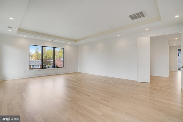 empty room featuring a raised ceiling, light wood-type flooring, recessed lighting, and baseboards