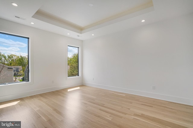 spare room featuring a raised ceiling, light wood-type flooring, recessed lighting, and baseboards