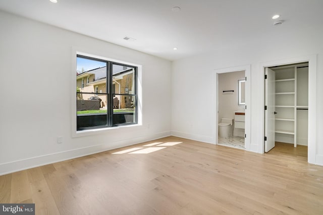 unfurnished bedroom featuring light wood-style flooring, baseboards, recessed lighting, a walk in closet, and connected bathroom