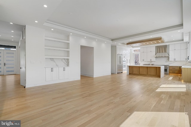 unfurnished living room featuring a raised ceiling, recessed lighting, light wood finished floors, and built in features