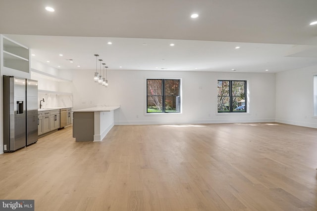 unfurnished living room with light wood-style floors, recessed lighting, a sink, and baseboards