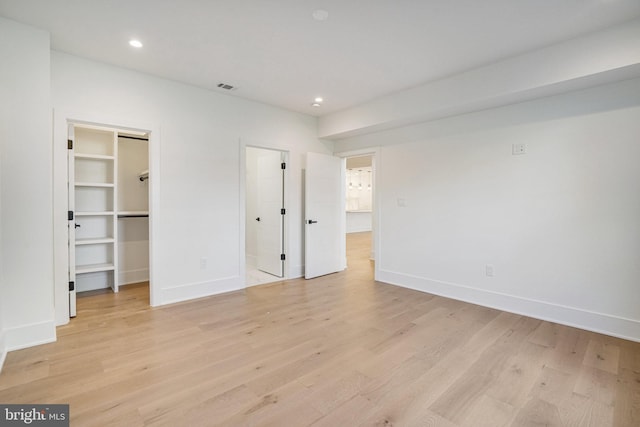 unfurnished bedroom featuring light wood finished floors, baseboards, a spacious closet, and recessed lighting