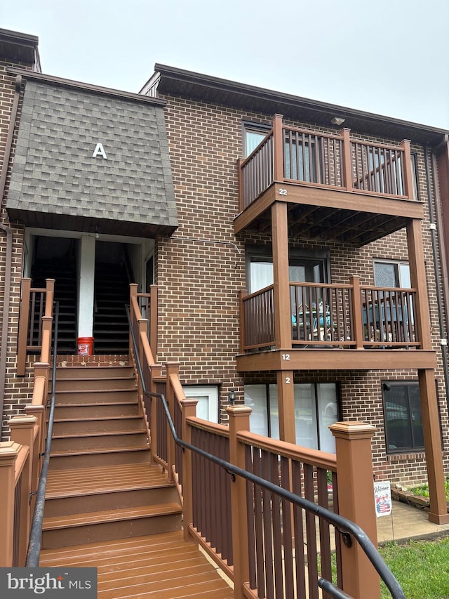rear view of house featuring brick siding, stairway, and a balcony