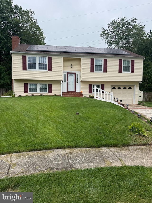 bi-level home with roof mounted solar panels, a garage, concrete driveway, a chimney, and a front lawn