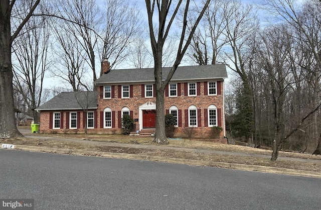 colonial inspired home featuring brick siding and a chimney