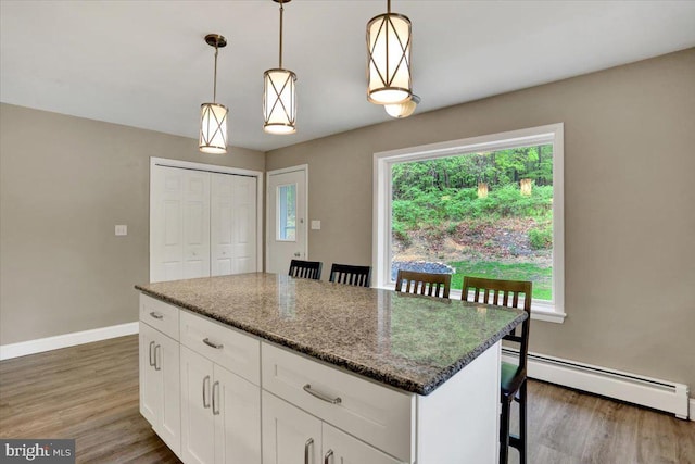 kitchen with a baseboard radiator, a kitchen bar, wood finished floors, and white cabinetry