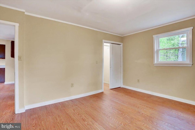 empty room with light wood finished floors, baseboards, and ornamental molding
