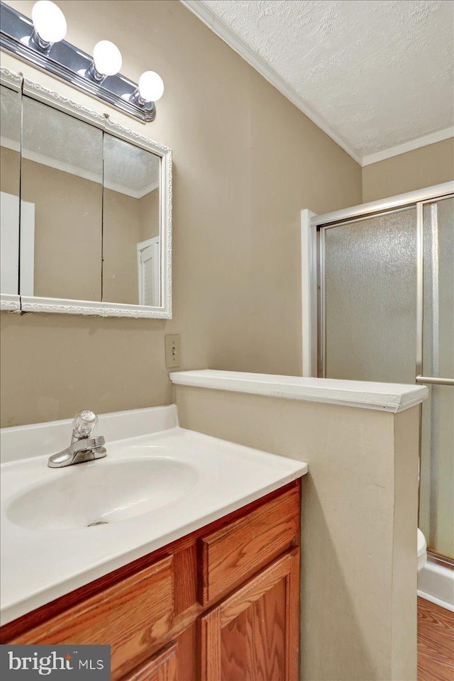 full bathroom featuring ornamental molding, a stall shower, vanity, a textured ceiling, and wood finished floors