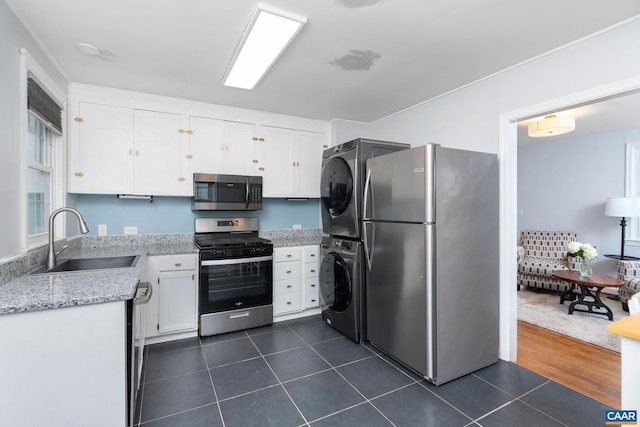 kitchen with appliances with stainless steel finishes, a sink, estacked washer and dryer, dark tile patterned flooring, and white cabinets