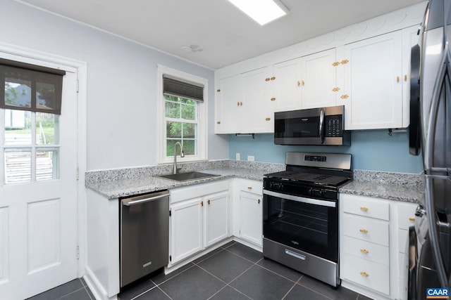 kitchen featuring appliances with stainless steel finishes, a sink, white cabinets, dark tile patterned floors, and light stone counters