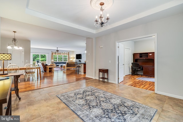 living area with a chandelier, a desk, baseboards, and a raised ceiling