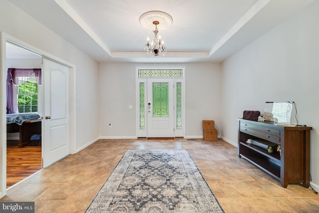 foyer entrance featuring a chandelier, a tray ceiling, stone finish floors, and baseboards
