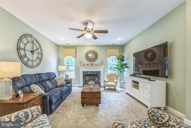 living room with a high end fireplace, a ceiling fan, baseboards, and light carpet