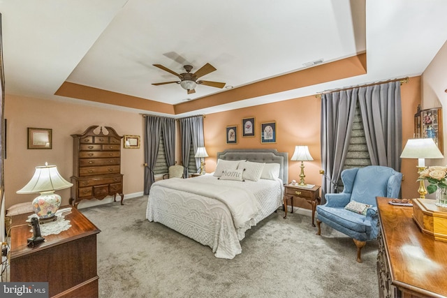 carpeted bedroom with a raised ceiling, baseboards, and ceiling fan