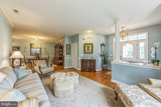 living area with ornate columns, a chandelier, wood finished floors, crown molding, and a wainscoted wall