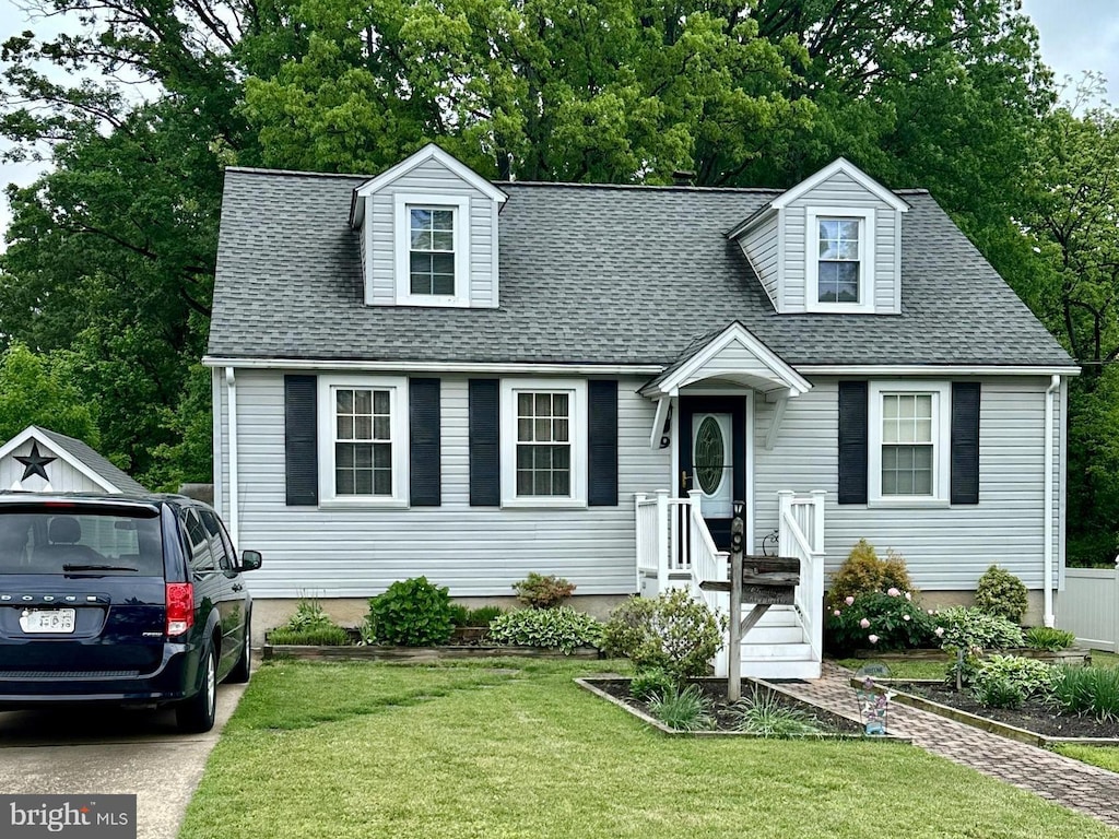 new england style home featuring a front lawn, a shingled roof, and view of scattered trees