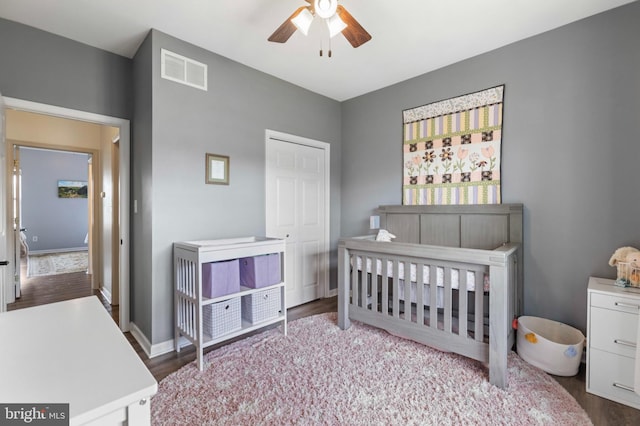 bedroom featuring wood finished floors, a nursery area, ceiling fan, a closet, and baseboards