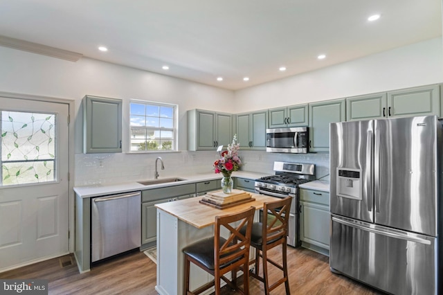 kitchen featuring appliances with stainless steel finishes, a sink, wood finished floors, tasteful backsplash, and recessed lighting