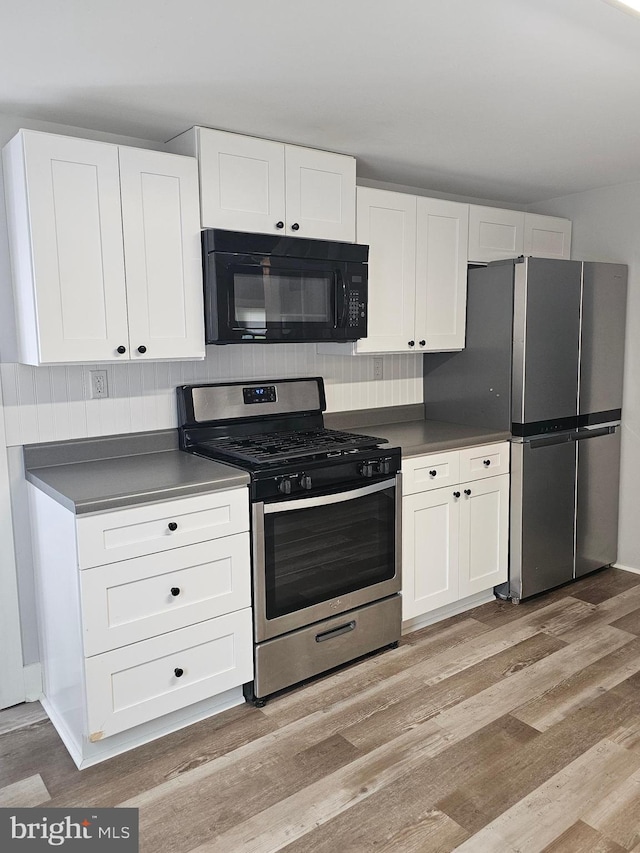 10992 Roxbury Rd, Orrstown, PA 17244 - kitchen featuring stainless steel appliances, light wood finished floors, white cabinetry, dark countertops, and backsplash
