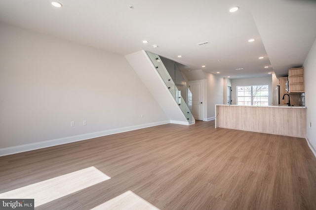 unfurnished living room with light wood-style floors, recessed lighting, stairs, baseboards, and a sink