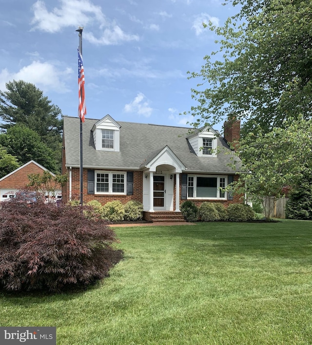 cape cod home with a front yard, a chimney, brick siding, and roof with shingles