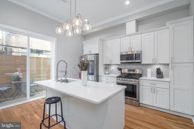 kitchen featuring stainless steel appliances, a sink, decorative backsplash, light wood-style floors, and crown molding