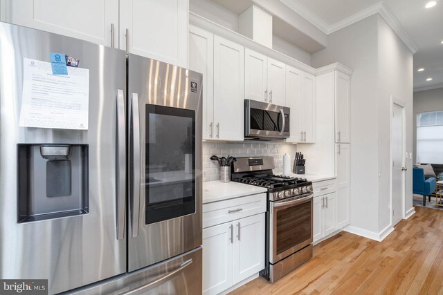kitchen with stainless steel appliances, crown molding, light countertops, white cabinetry, and light wood finished floors