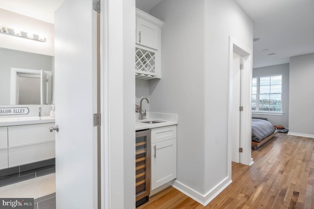 indoor wet bar featuring beverage cooler, light wood finished floors, and baseboards