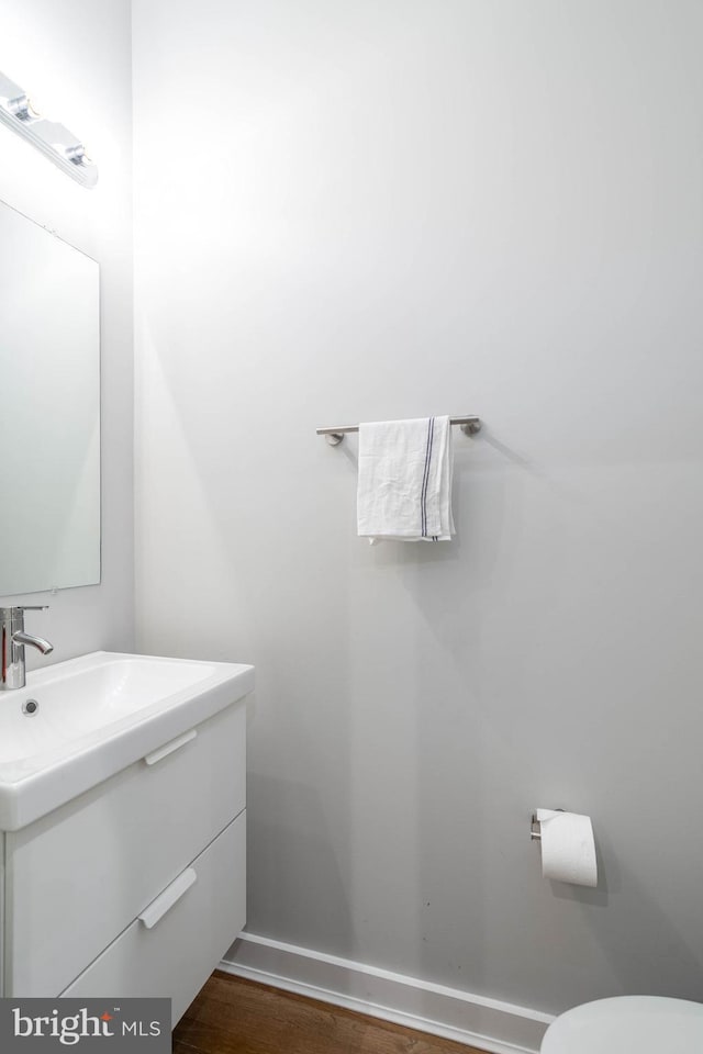 half bathroom featuring vanity, wood finished floors, baseboards, and toilet