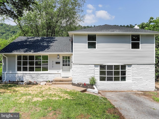 split level home with stone siding, a front yard, and a shingled roof