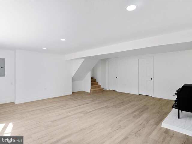 finished below grade area with stairs, light wood-type flooring, electric panel, baseboards, and recessed lighting