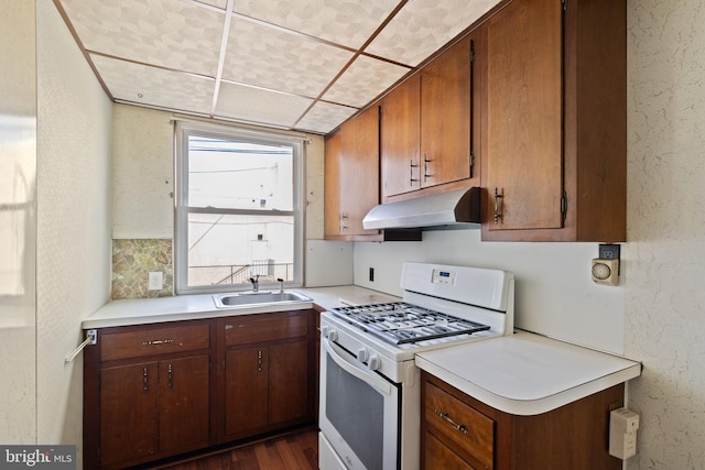 6602 Revere St, Philadelphia, PA 19149 - kitchen with under cabinet range hood, white range with gas stovetop, a sink, light countertops, and brown cabinets