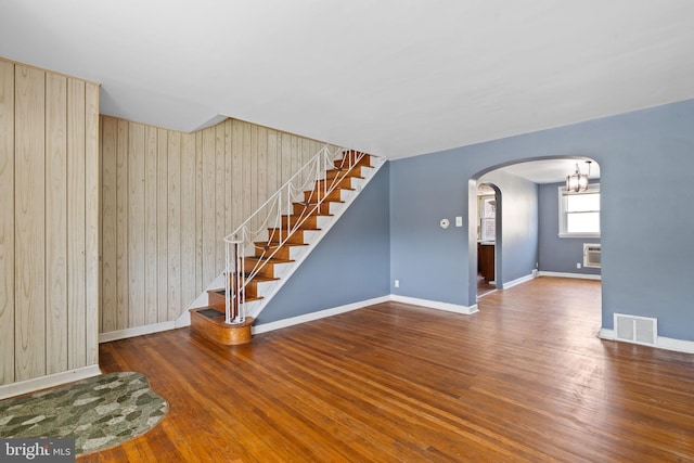 6602 Revere St, Philadelphia, PA 19149 - unfurnished living room featuring arched walkways, baseboards, wooden walls, stairway, and wood finished floors