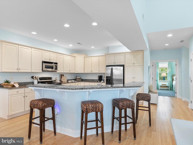 32561 Heron Cir Unit 13, Bethany Beach, DE 19930 - kitchen featuring appliances with stainless steel finishes, a breakfast bar, light wood-style flooring, recessed lighting, and dark stone counters